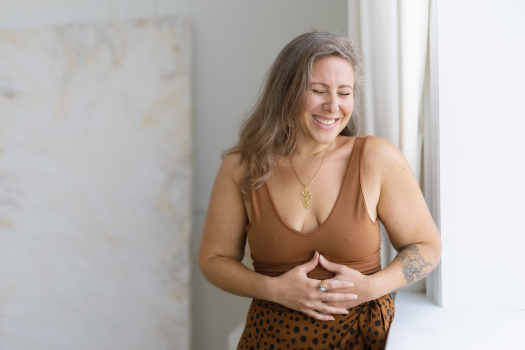 Woman by a window with hands on her abdomen. 