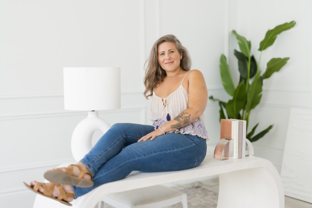 Jaime Verk sitting on a desk relaxed with a plant behind. 
